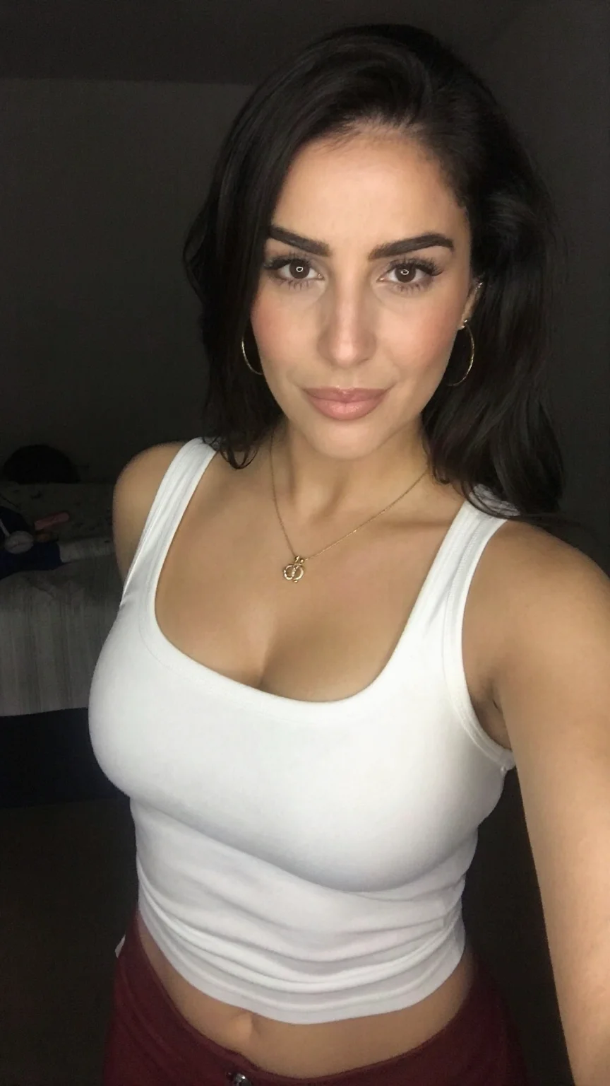Middle-eastern woman in white tank top bedroom selfie smiling